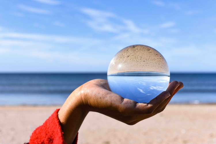 A glass globe being held in the hand on a person. In the background is a beach