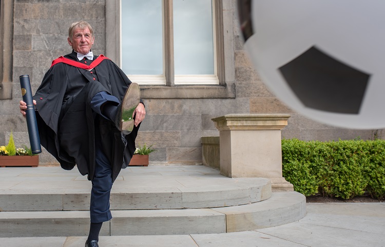 Sir Kenny Dalglish kicks a football after graduation ceremony