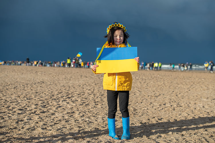 Girl in yellow jacket on beach holding Ukraine flag
