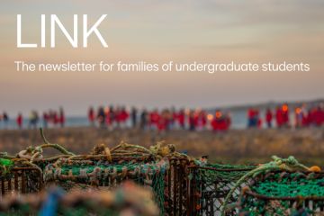 An artistic, out-of-focus image showing students in red gowns on a pier with a sunset beyond and lobster creels in the foreground.