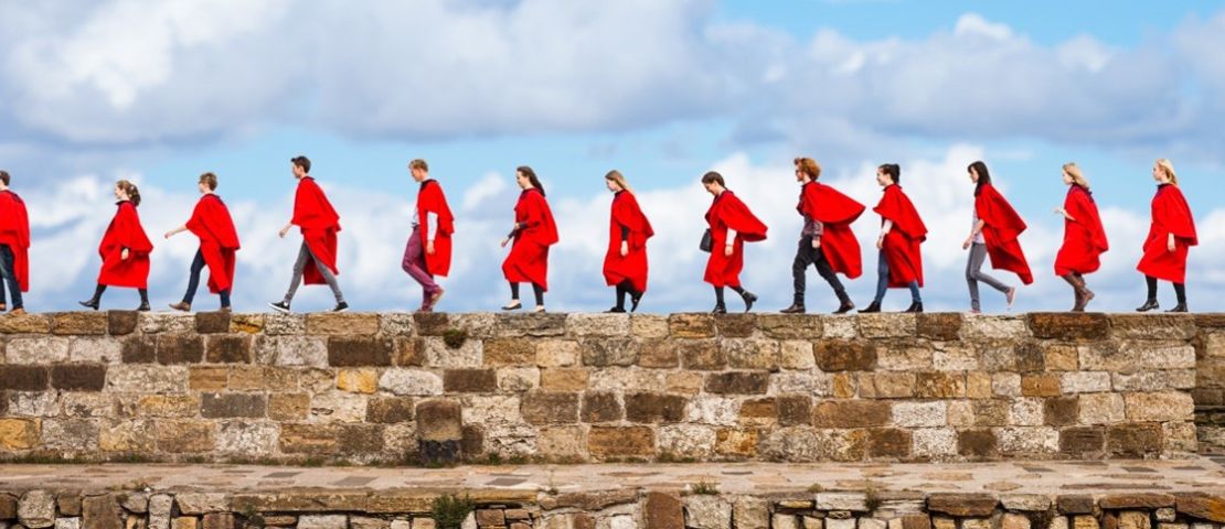 Students wearing red gowns walking along the pier