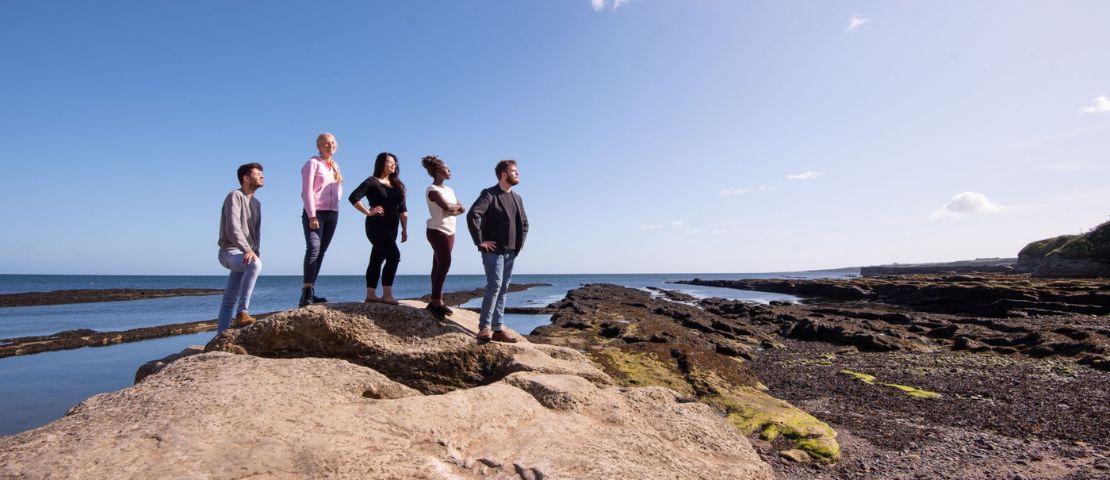 students standing on rocks looking at sea