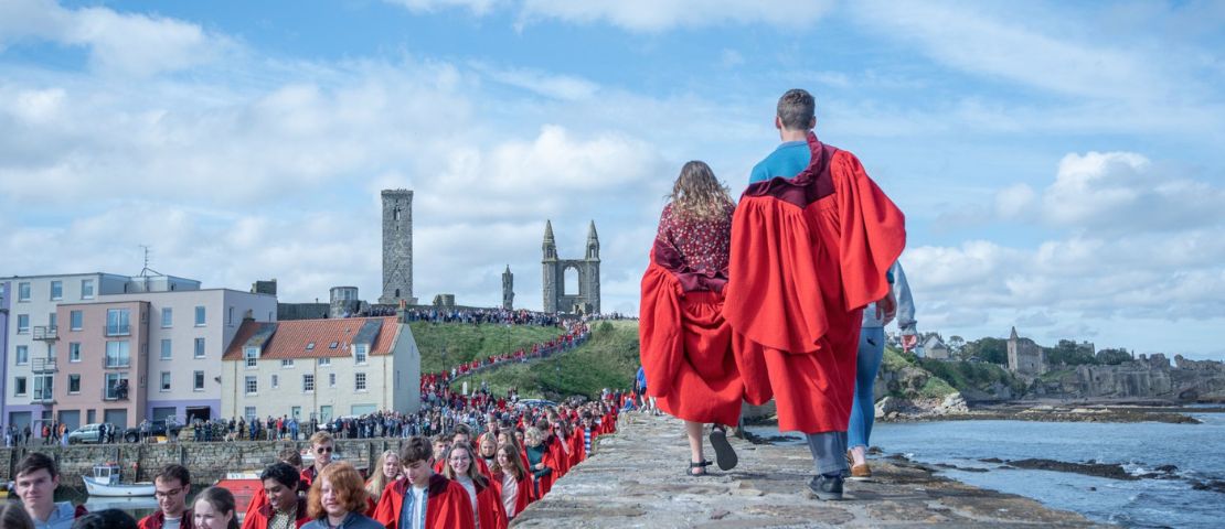 Students walking along pier wearing red gowns