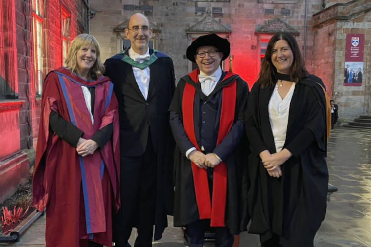 Picture of 4 people in academic robes in front of historic buildings