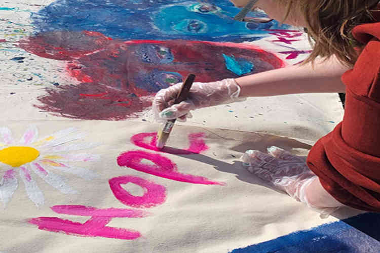A child uses a paintbrush to write the word hope on a piece of fabric