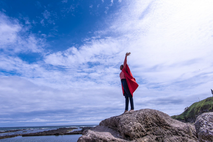 Student in red gown standing on rock overlooking the sea