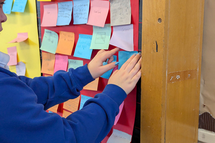 A schoolboy in a blue jumper adds another sticky note to a board