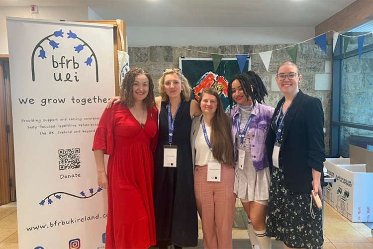 Five women standing in front of a roller banner advertising the BFRB charity.