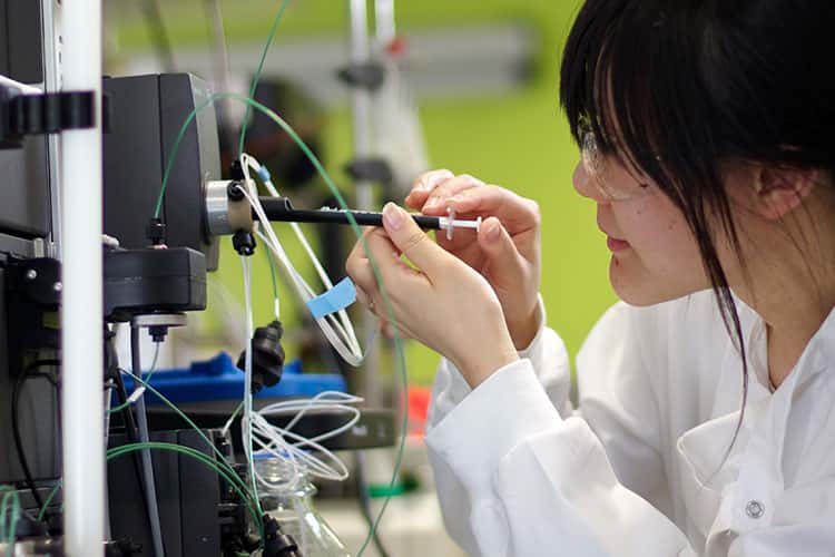 Woman in lab coat injects syringe into machinery