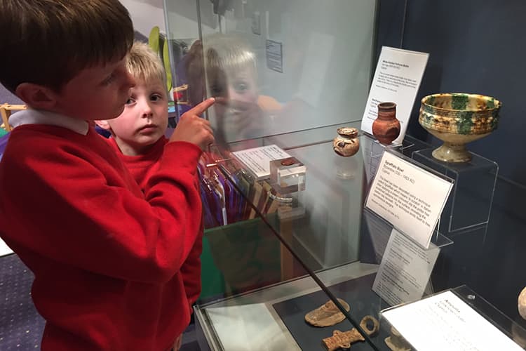 Two boys pointing at small pots which are in a glass case
