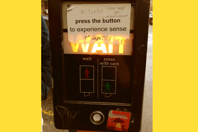 street crossing sign showing 'WAIT' and a sticker saying 'press the button to experience sense of agency' with graffiti 'actants! Labour says yes we are a network'