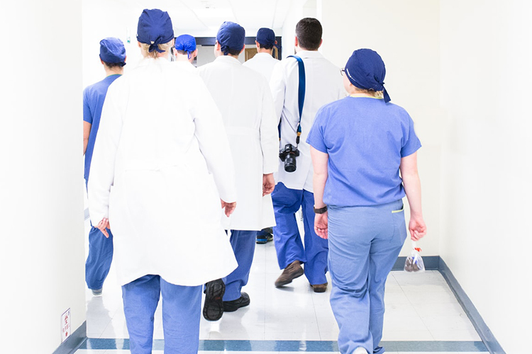 medical team of seven people, one with a camera over their shoulder, walking away down a hospital corridor; credit Luis Melendez on unsplash
