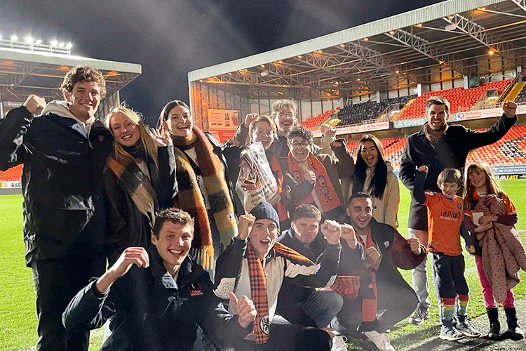 students and staff from Leadership Development class shown on the pitch at DUFC with bright lights on the empty stands in the background
