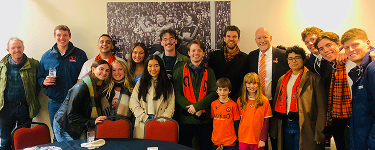 students and staff from Leadership Development class with members of DUFC, in front of a large b/w photo of a football match