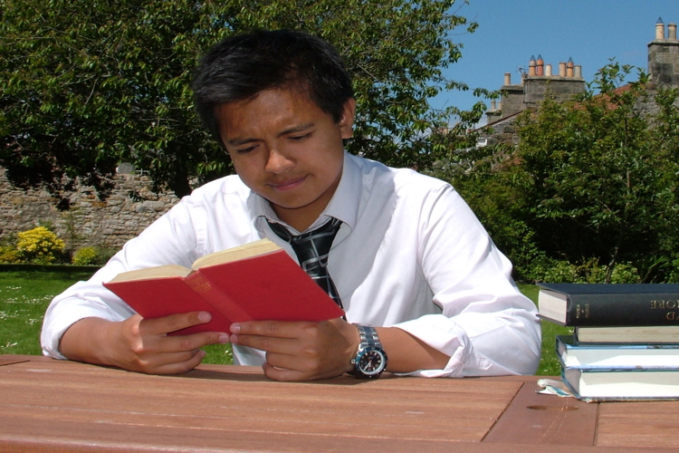 Student sitting outside at a table reading