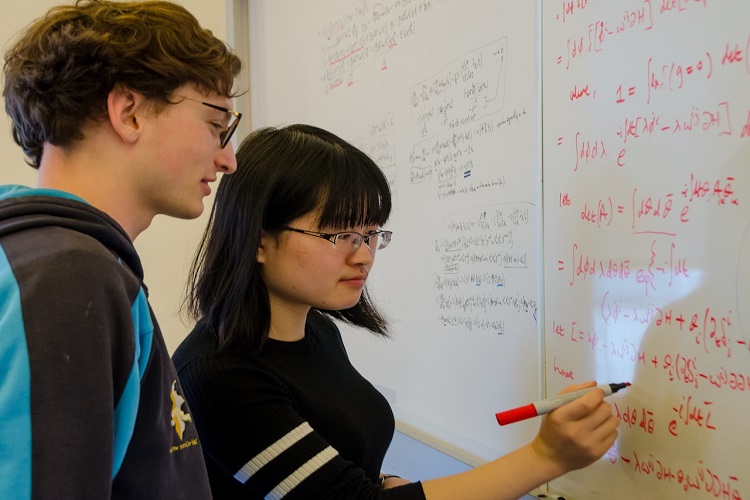 Two physics students discussing at a whiteboard.