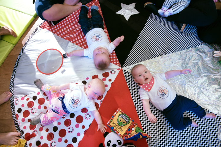 Babies gathered in a circle on a multicoloured sensory mat