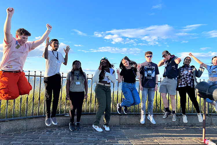 A group of students jump into the air on cobblestones.