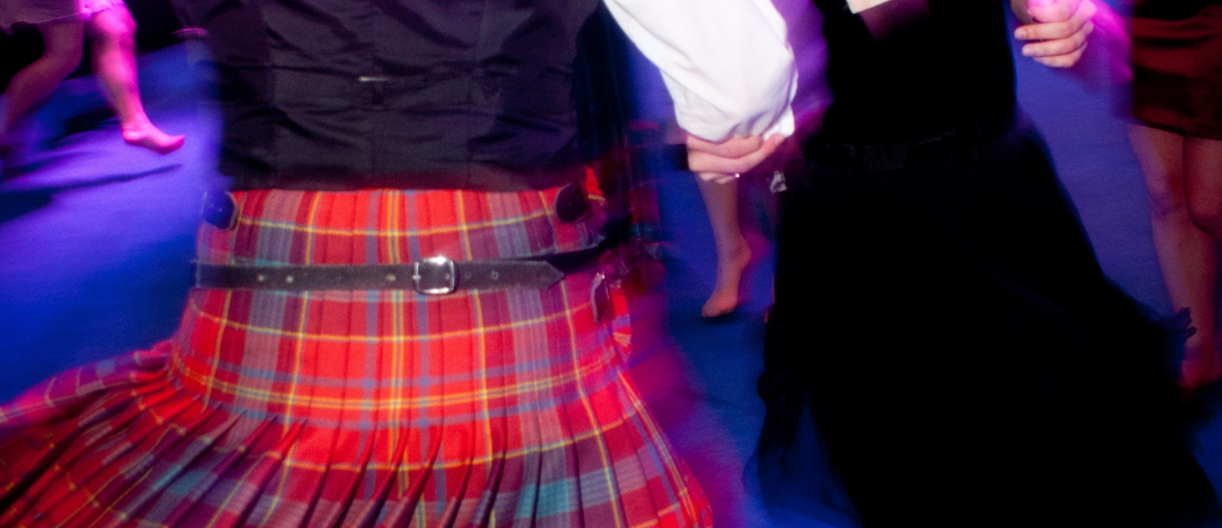 Two people dancing together at a formal event. One person is wearing a kilt