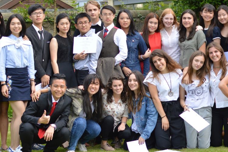 A large group of happy students outside. The front row are knelling down and the row behind them are standing up.