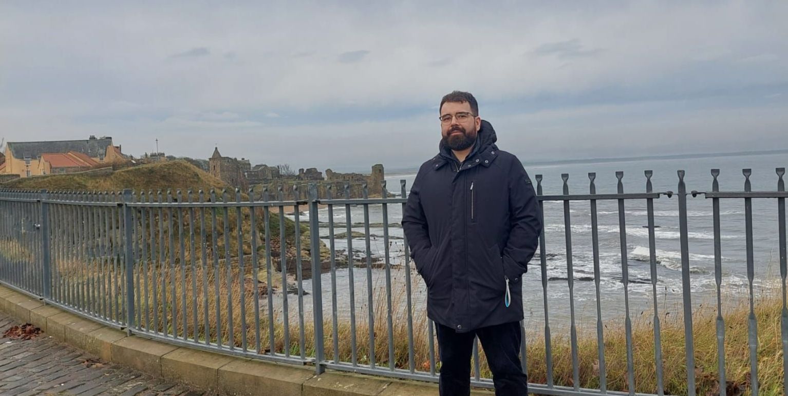 ndrei poses for a photo on the shores of St Andrews - the sea and castle can be seen in the background ndrei poses for a photo on the shores of St Andrews - the sea and castle can be seen in the background