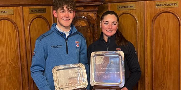 Ollie and Caitlin stand holding their Order of Merit trophies. The pair are wearing the Saints Golf branded jumpers and smiling at the camera Ollie and Caitlin stand holding their Order of Merit trophies. The pair are wearing the Saints Golf branded jumpers and smiling at the camera