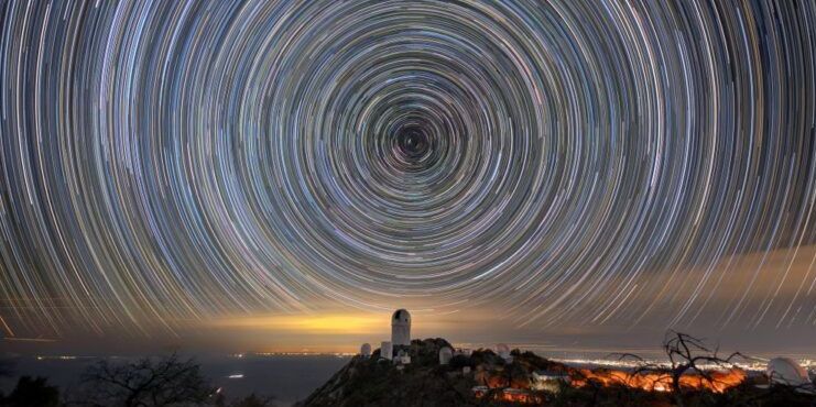 Circles of light on the night sky. A telescope dome atop a mountain is below the center of the circle. Circles of light on the night sky. A telescope dome atop a mountain is below the center of the circle.