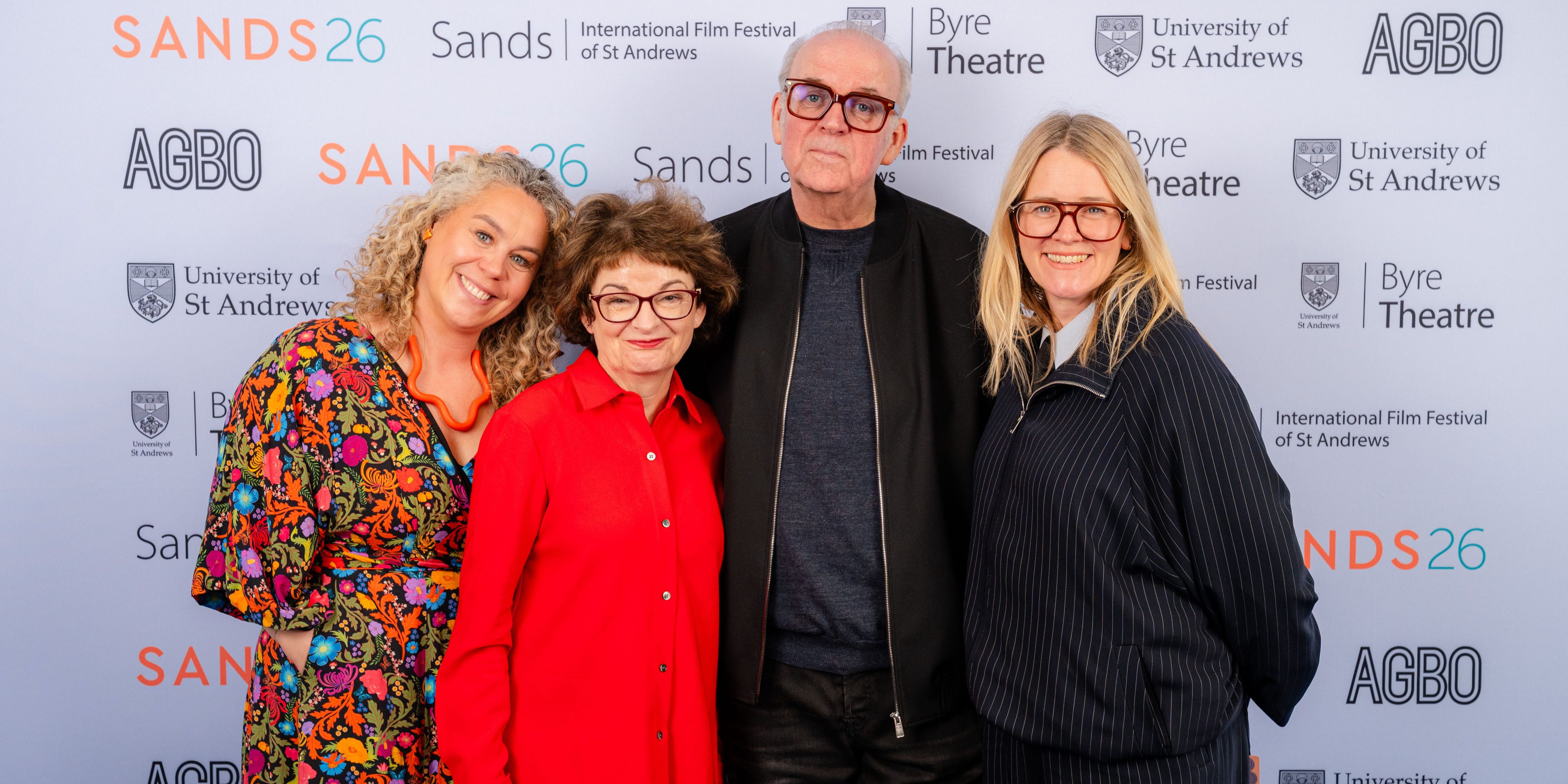 Ania Trzebiatowska, Professor Dame Sally Mapstone, Craig Armstrong, and Edith Bowman pose smiling for a group photo in front of the Sands 26 press wall Ania Trzebiatowska, Professor Dame Sally Mapstone, Craig Armstrong, and Edith Bowman pose smiling for a group photo in front of the Sands 26 press wall