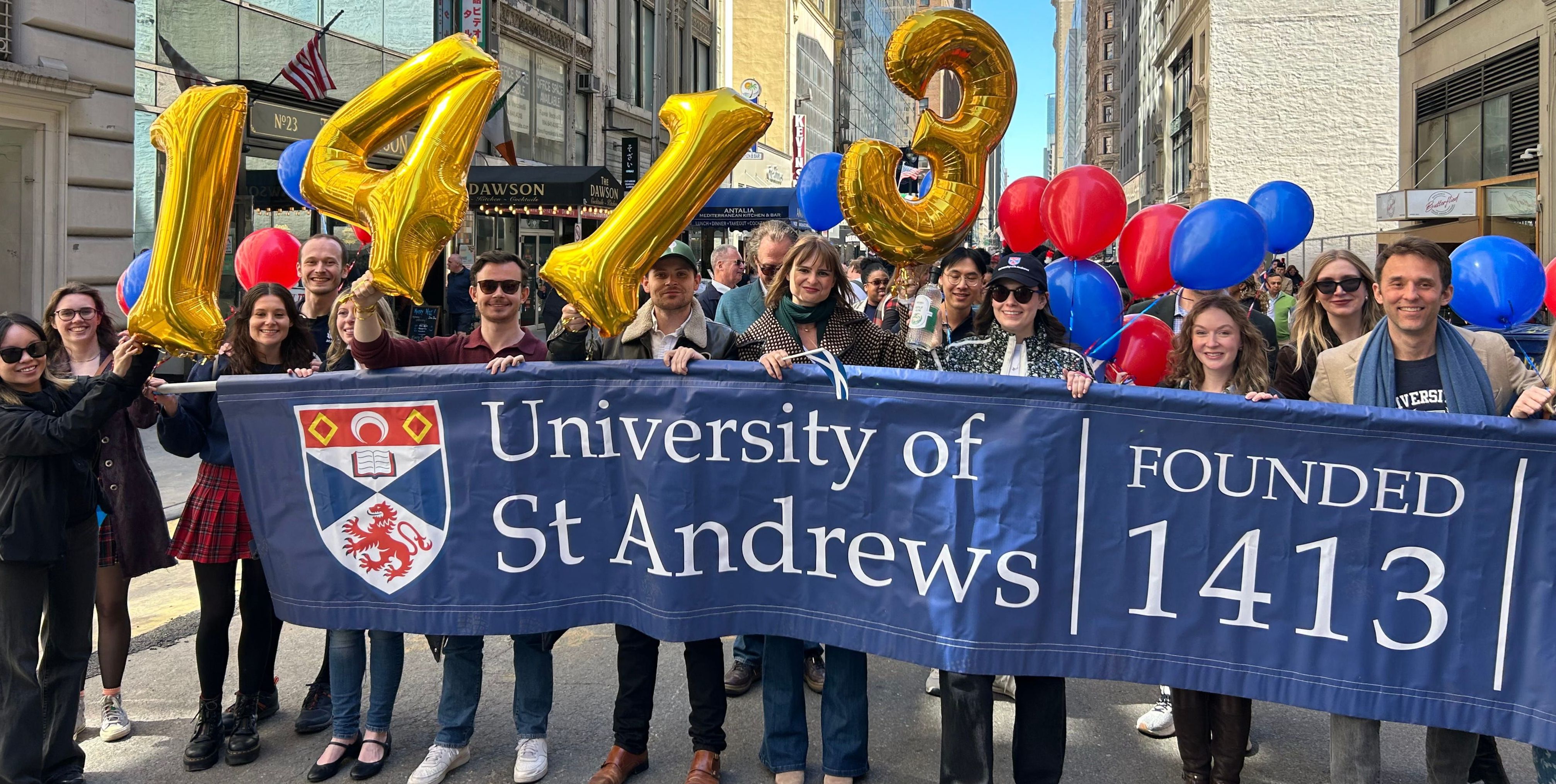 The New York Alumni Club stand holding a banner that reads 'University of St Andrews, founded 1413' the group holds gold foil number balloons of '1413' and red and blue balloons The New York Alumni Club stand holding a banner that reads 'University of St Andrews, founded 1413' the group holds gold foil number balloons of '1413' and red and blue balloons