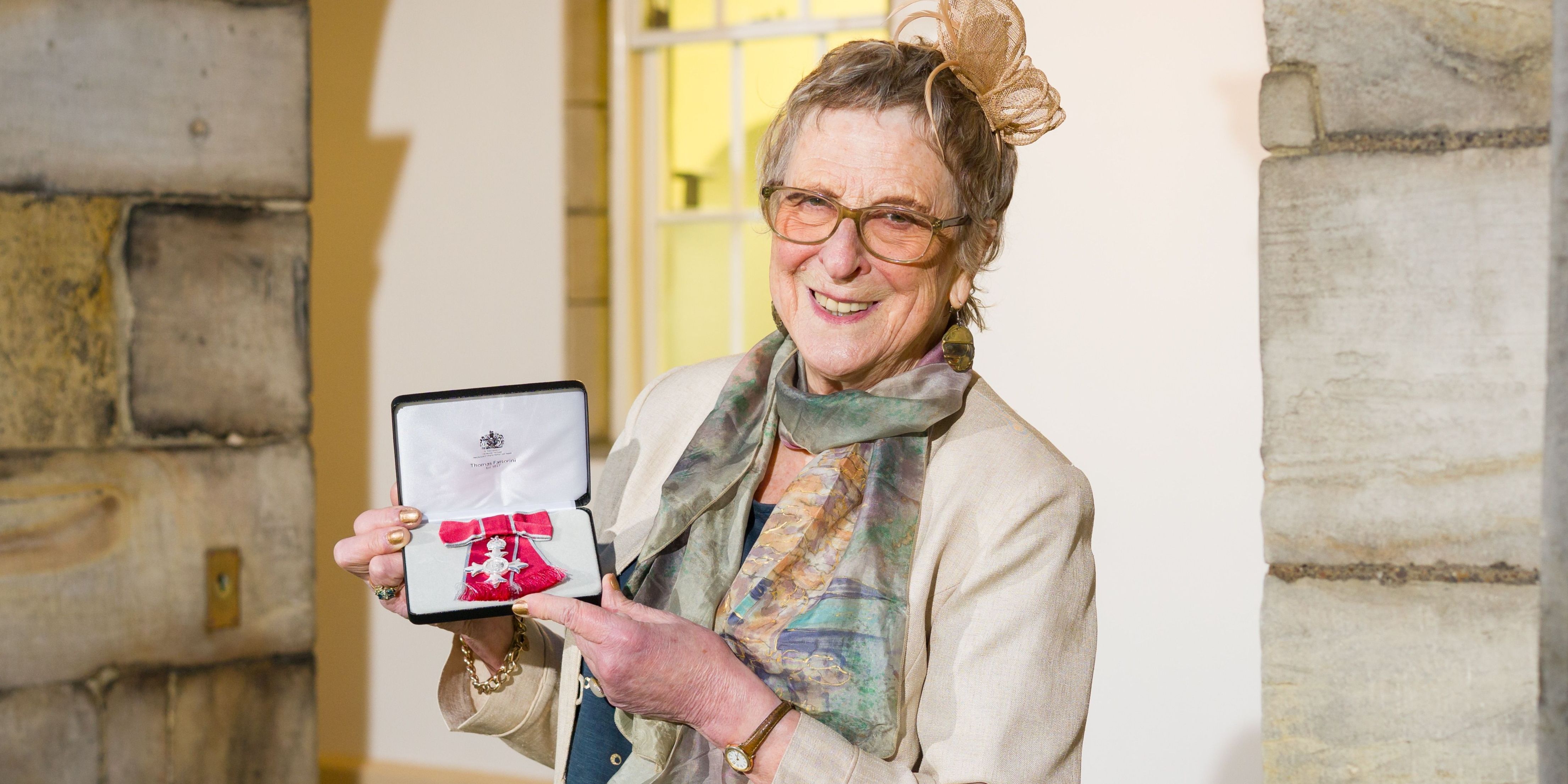 Bridget smiles at the camera, she is proudly holding her MBE. Bridget smiles at the camera, she is proudly holding her MBE.