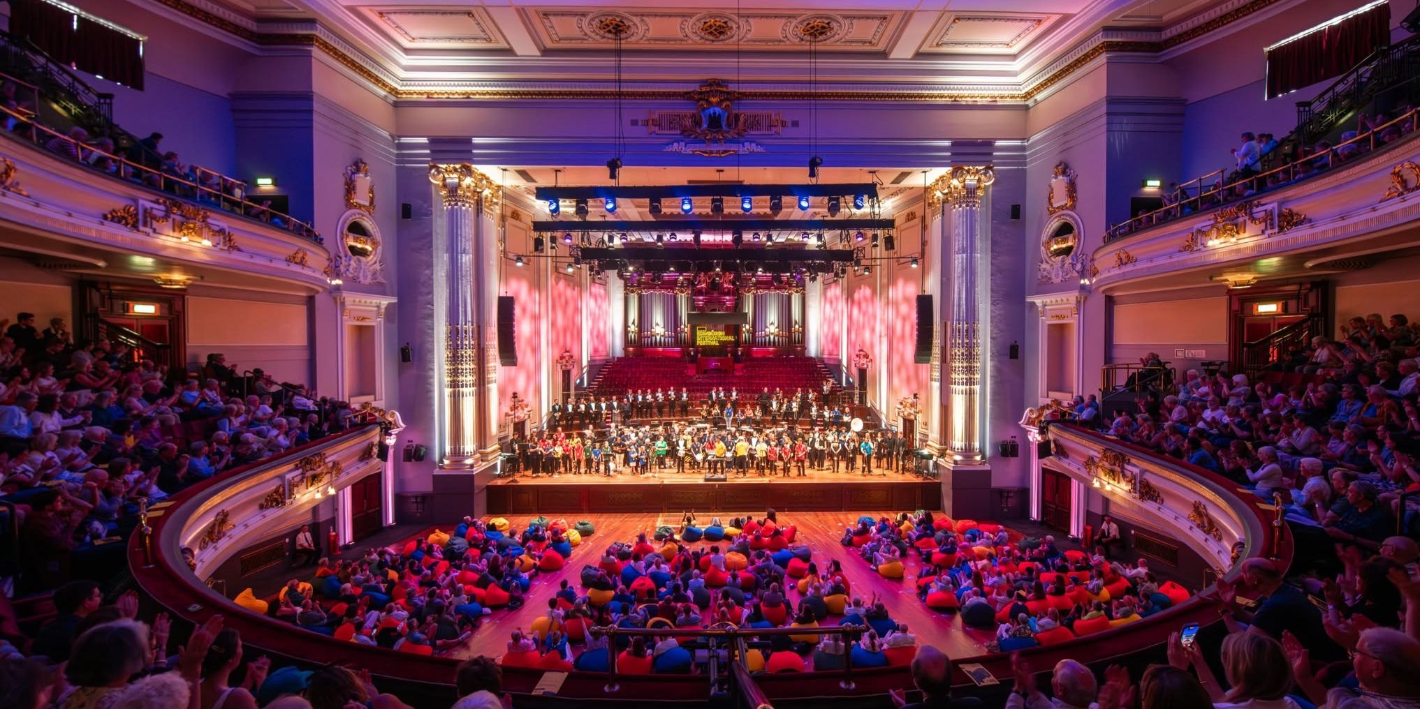 A full auditorium with a large group of musicians on stage A full auditorium with a large group of musicians on stage