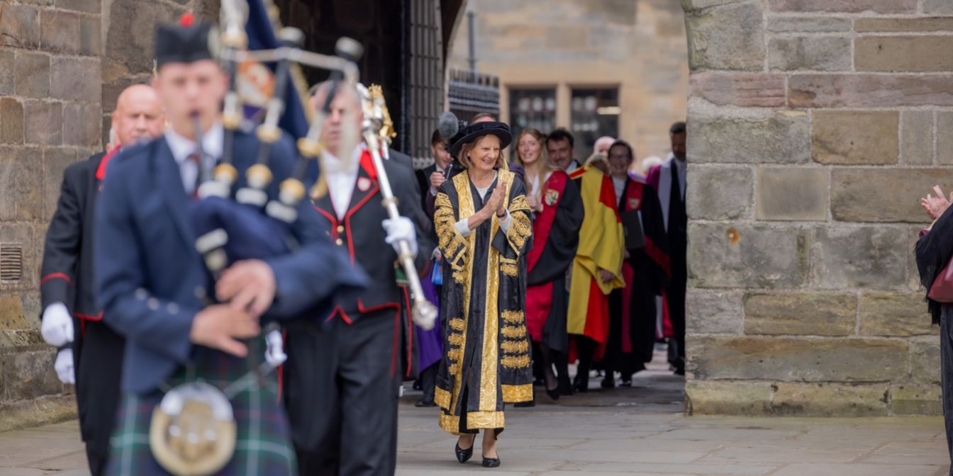 Chancellor Dame Anne Pringle, in ceremonial dress, is pictured entering the archway in St Salvator's Quad during a graduation procession. She is smiling and clapping as she enters the quad. The Chancellor's piper can be seen in the foreground of the image, followed by the University macebearers. Chancellor Dame Anne Pringle, in ceremonial dress, is pictured entering the archway in St Salvator's Quad during a graduation procession. She is smiling and clapping as she enters the quad. The Chancellor's piper can be seen in the foreground of the image, followed by the University macebearers.