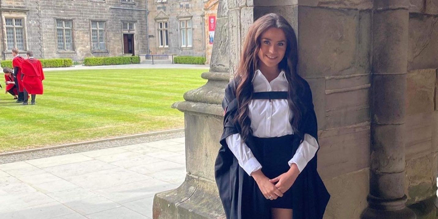 Laura poses for a photo in her graduation gown and academic dress. She stand in the cloisters, with a view of St Salvator's Quad in the background. Laura poses for a photo in her graduation gown and academic dress. She stand in the cloisters, with a view of St Salvator's Quad in the background.