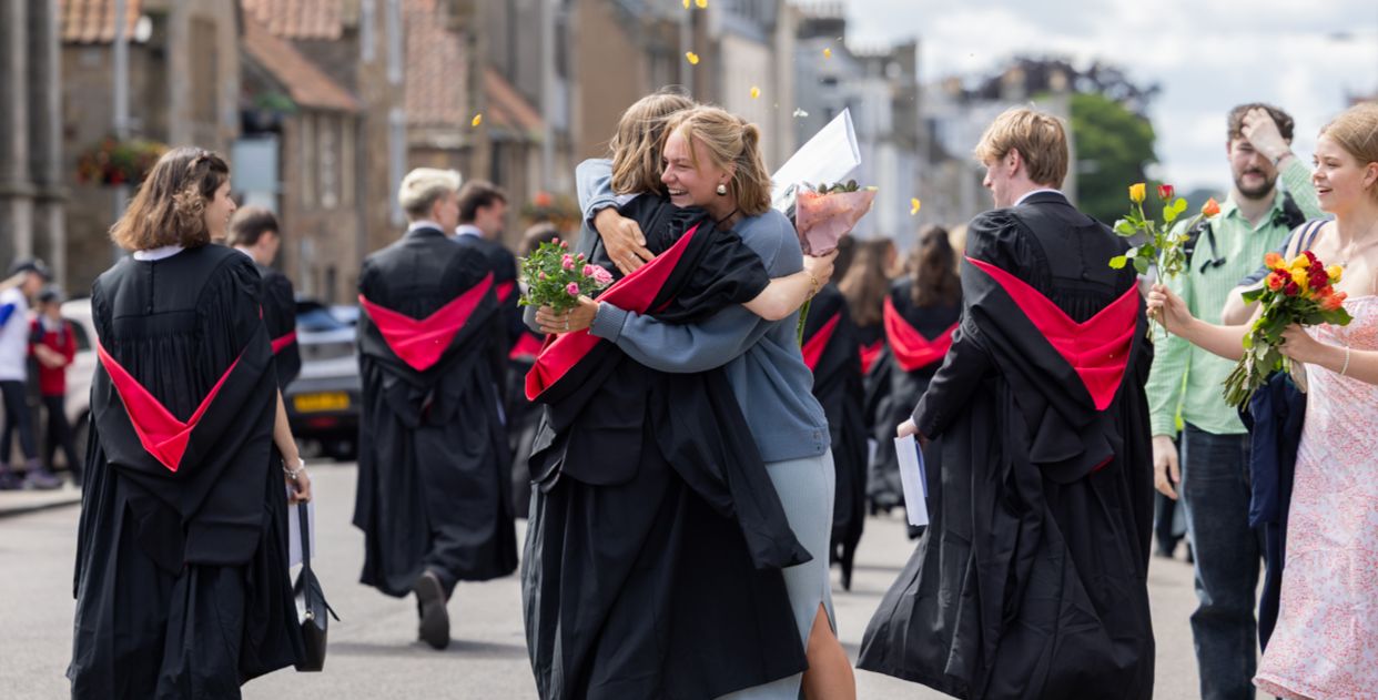 A graduate hugs a friend on North street during the graduation procession. Both the friend and graduate are holding bouquets of flowers. Yellow flower petals are thrown into the air surrounding the pair A graduate hugs a friend on North street during the graduation procession. Both the friend and graduate are holding bouquets of flowers. Yellow flower petals are thrown into the air surrounding the pair