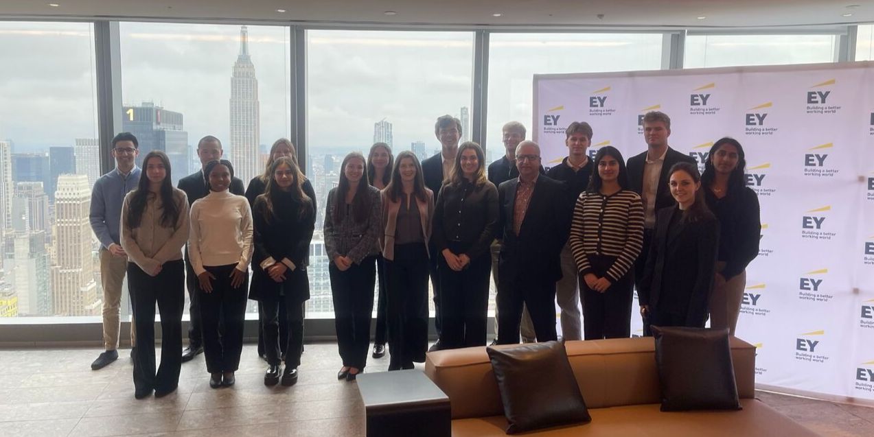 Group of students stand smiling in front of EY branding and New York City skyline Group of students stand smiling in front of EY branding and New York City skyline