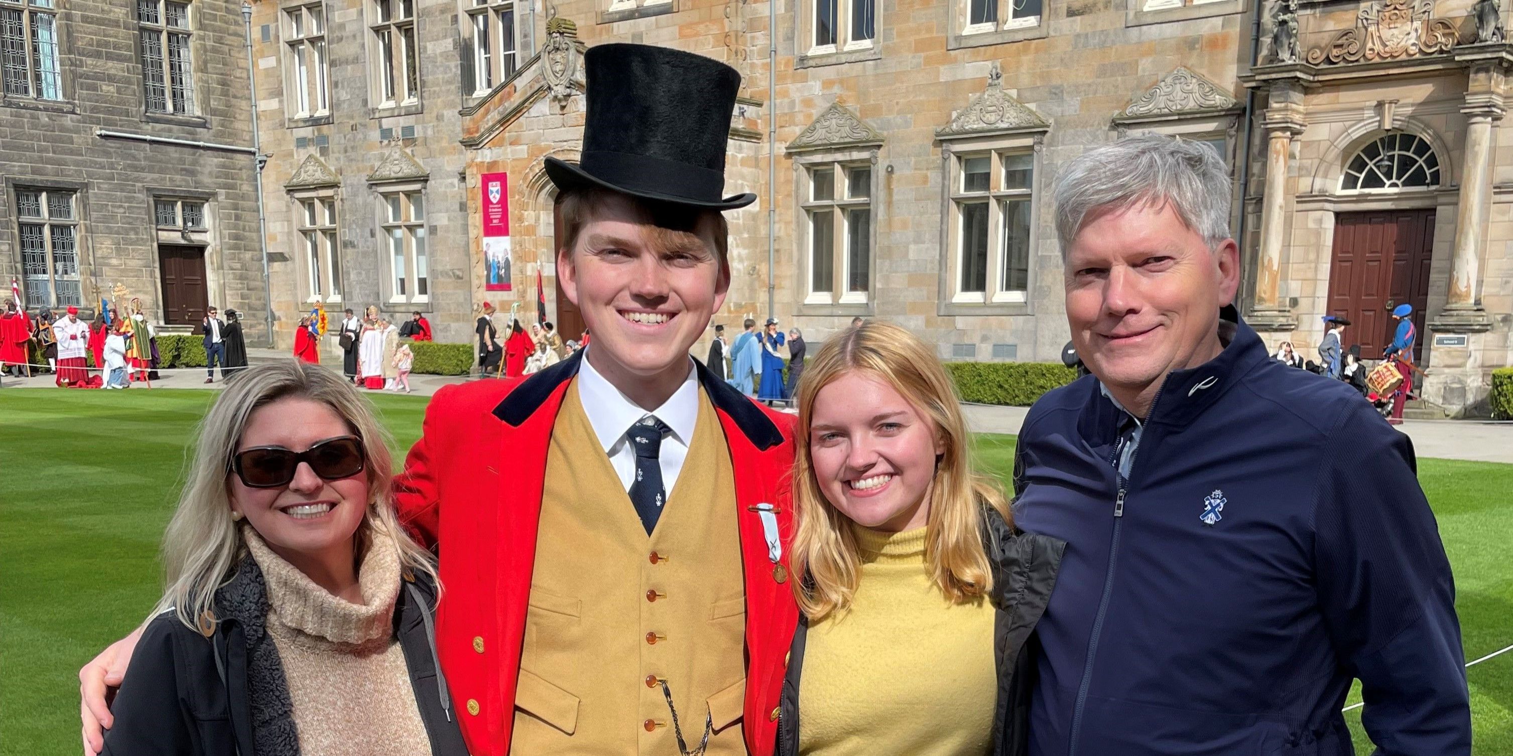 Four people, Edward, Izzie, Carrie, and Lyon, stand smiling for a photo in St Salvator's Quad. Lyon is wearing historical dress and a top hat as his character 'Sir Hugh Lyon Playfair' Four people, Edward, Izzie, Carrie, and Lyon, stand smiling for a photo in St Salvator's Quad. Lyon is wearing historical dress and a top hat as his character 'Sir Hugh Lyon Playfair'