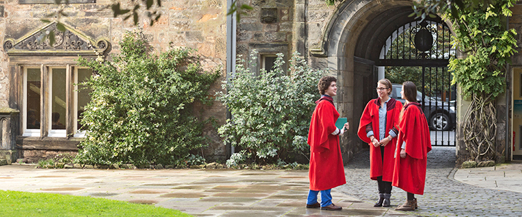 Three students wearing red gowns stand in St Marys quad